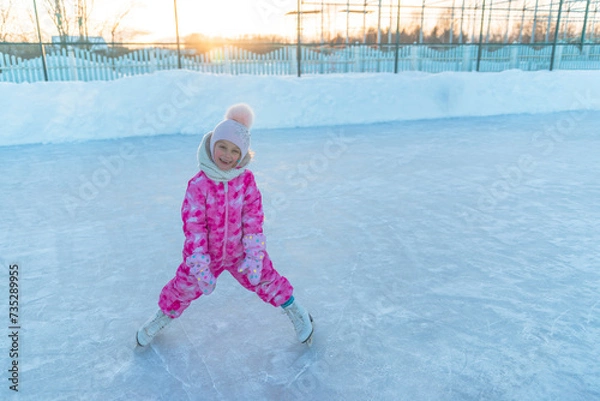 Fototapeta A little girl of 5 years old sits on a tubing and relaxes after skating on white figure skates at the skating rink in winter.