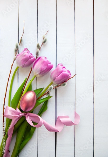 Fototapeta Pink tulips, willow branches and a golden egg on a white wooden table. Easter card.