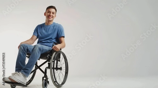 Obraz white man with a physical disability smiling and sitting in a wheelchair dressed in jeans, a blue t-shirt, positioned against a white background, Fashion mockup, Lifestyle, Stylish studio background