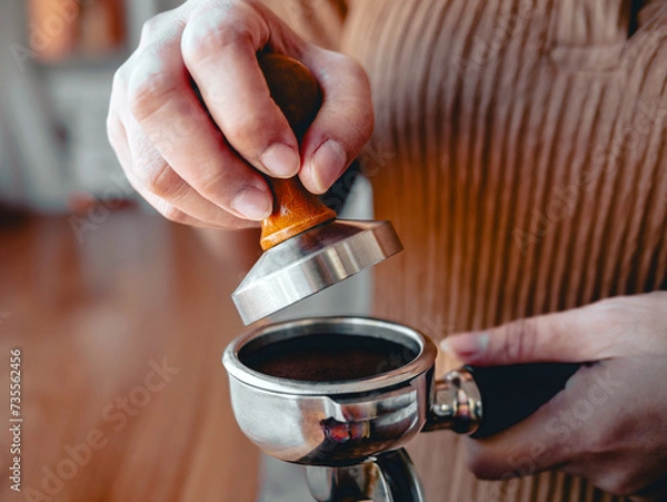 Fototapeta Close-up of hand Barista cafe making coffee with manual presses ground coffee using tamper at the coffee shop