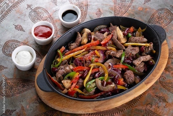 Fototapeta Popular Tex-Mex dish made from grilled meat, usually beef or chicken, which is served on a sizzling hot skillet along with grilled onions and peppers. The meat and vegetables are served with warm tort