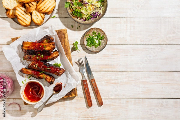 Fototapeta Grilled and smoked ribs with barbeque sauce on a carving board served with coleslaw salad and green onions. Top view, wooden background.