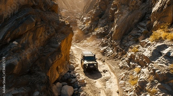 Fototapeta Overhead view of a new heavy car driving through a rocky canyon, navigating challenging terrains effortlessly.