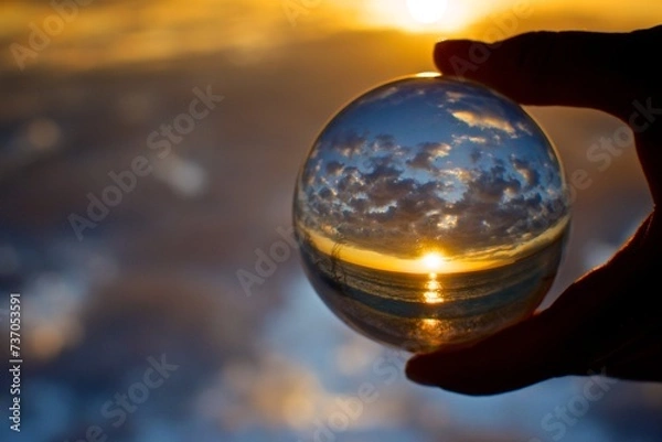 Fototapeta A woman's hand holds a crystal ball in which you can see a beautiful sunrise in the ocean upside down