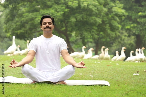 Obraz Happy Indian man doing yoga early morning in a tranquil environment surrounded with lush green serene atmosphere. high concentration level. 