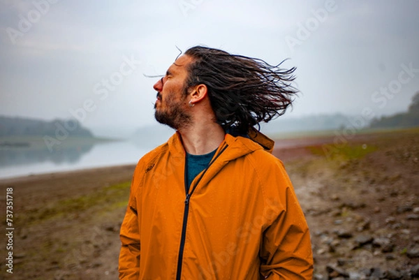 Fototapeta Long haired man standing in a rain soaked landscape shaking his head and smiling 