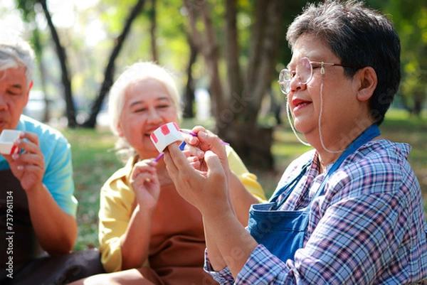 Fototapeta Art activities for the elderly. A group of elderly people sit and paint pots in the garden outside. They are happy. Living happily in retirement. art therapy