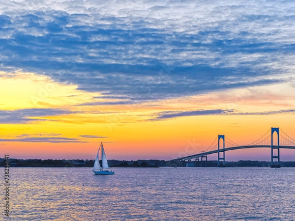 Fototapeta Dramatic beautiful sunset with Claiborne Pell Newport Bridge sailboat and clouds Newport, Rhode Island, USA, a popular New England holiday vacation destination in summer and fall. 