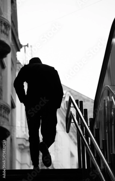 Fototapeta Blurry silhouette of a young man walking alone up the city subway stairs with hands in pockets