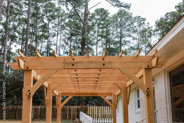 Fototapeta The rear back exterior of a newly painted and renovated white brick ranch style house with a large yard and a newly built wood arbor pergola for shade