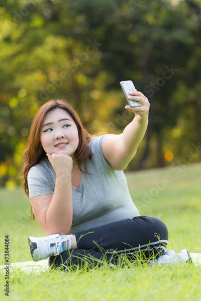 Obraz beautiful obese women sitting on grass and taking selfie