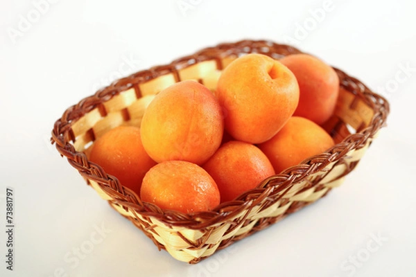 Fototapeta Ripe apricots in a wicker basket isolated on a white background