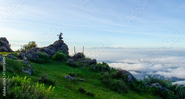 Fototapeta Persona con los brazos abiertos en una roca sobre las nubes