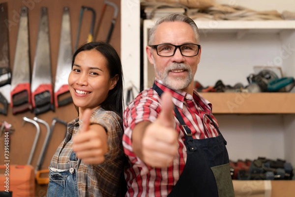 Fototapeta Group of carpenter teamwork working at carpentry shop with tools shelves background, happiness senior entrepreneur carpenter thumbs up at workshop. Builder, construction, craftsman, timber, lumber