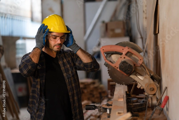 Fototapeta Young carpenter wearing earmuffs before cutting wood plank by circular saw machine at carpentry shop, security protection. Joiner, builder, maker of furniture handmade at workshop