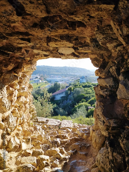 Fototapeta View through the window of an ancient stone tower onto a natural landscape.