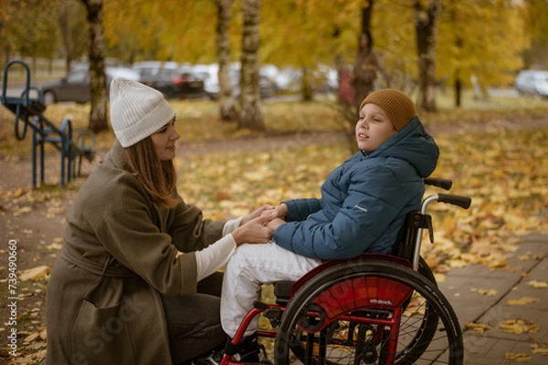 Fototapeta a 10-year-old boy in a wheelchair walks in the fall with his mother on the street with a dog on the playground. High quality photo