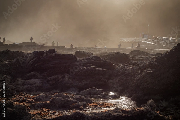 Obraz Rocks in the foreground, with people enjoying an end-of-day walk on the beach