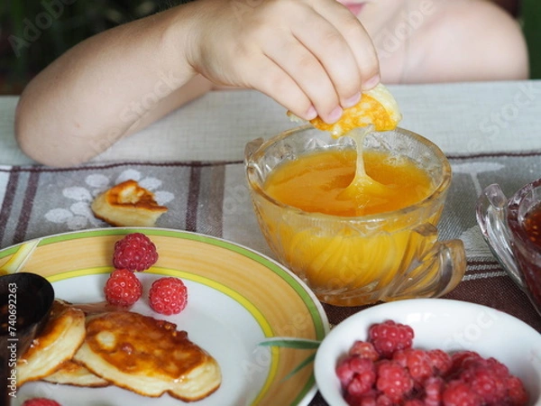 Fototapeta Summer children is breakfast. The child eats pancakes with honey with his hands. Baby food and allergies.