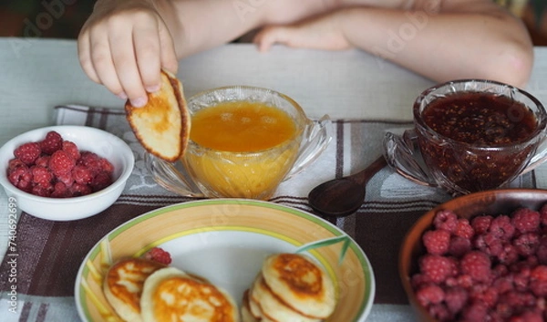 Fototapeta Summer children is breakfast. The child eats pancakes with honey with his hands. Baby food and allergies.