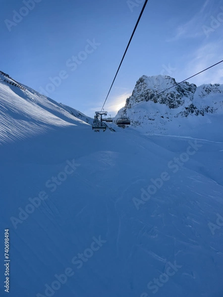 Obraz Chairlift with sun peeking out behind the hills in Lech am Arlberg in wintertime