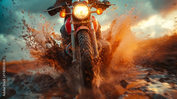 Obraz A motorcycle crossing a mud puddle, its tires spraying the air