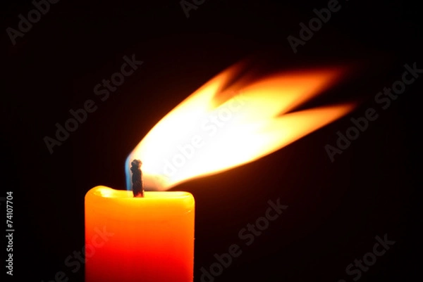 Obraz Orange candle burning on a black background