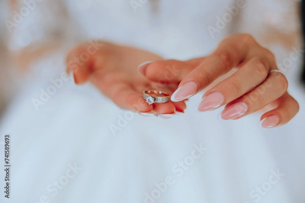Fototapeta Close-up of an elegant diamond ring on a woman's finger with a modern manicure, sunlight. Love and wedding concept. Soft and selective focus.