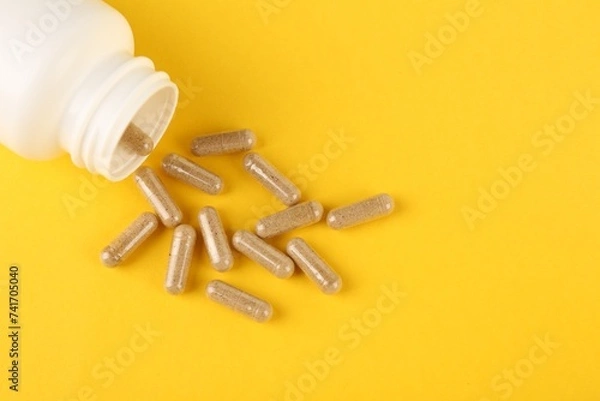 Obraz White medical bottle and vitamin capsules on yellow background, top view. Space for text