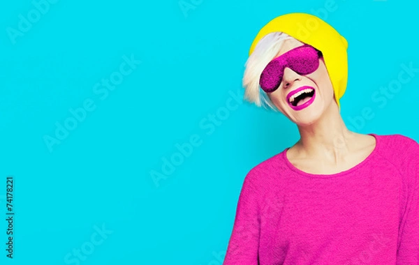 Obraz blond happy girl with a stylish cap and sunglasses on bright bac