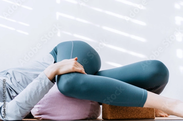 Fototapeta Woman doing yin yoga passive supine twists with bolster and cork block
