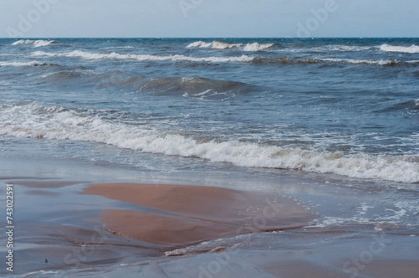 Obraz Seascape on Baltic Sea. Foaming waves running towards shore are depicted. Sandy shore is decorated with delicate traces of water, creating  natural pattern.
