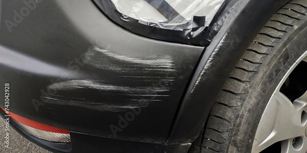 Fototapeta Plastic car bumper with a scratch, under the black bumper of a car.