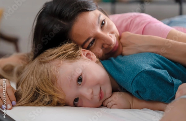 Fototapeta A little boy lying down on bed with his mom over him, listen daddy tell a fairy tale story before going to bed. A little smile son feeling happy when his parents stay with him before he sleeps.