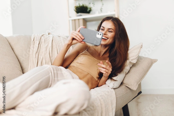 Obraz Relaxed Woman Sitting on a Cozy Couch, Holding Mobile Phone and Smiling