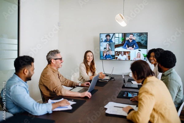 Obraz A lively and productive team meeting is captured where colleagues are connected via a large screen, showcasing a blend of in-person and remote collaboration. Virtual meeting concept
