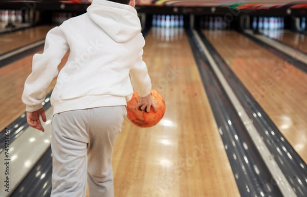 Obraz Rear view of boy holding bowling ball while standing in bowling alley in shooting position