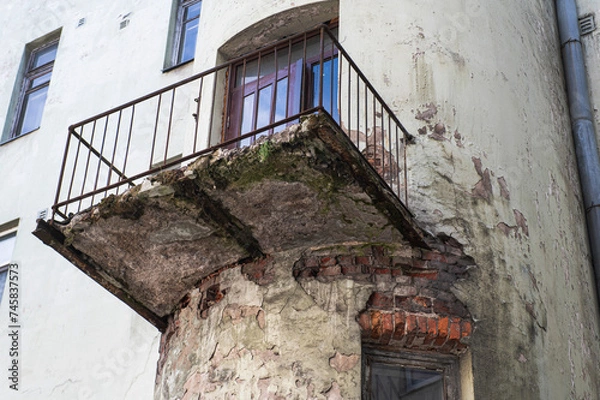 Obraz dangerous balcony in an old residential building. The concrete slab is almost destroyed, exposing rusty reinforcement. The plaster of the wall is also damaged exposing the brickwork