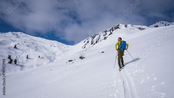 Fototapeta Man on mountain ski tour in the snow on sunny day, looking at the winter panorama around.