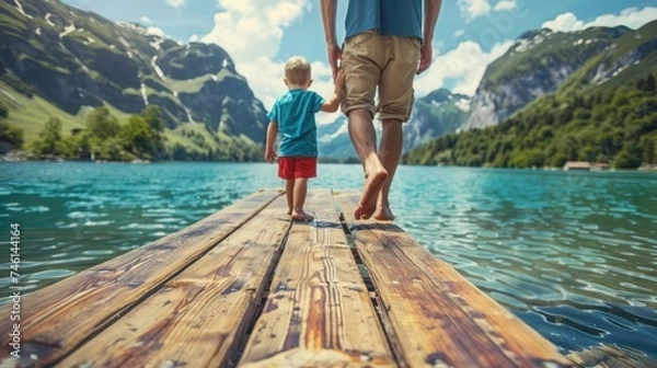 Fototapeta Father and son swung their legs from the wooden pier on mountain lake