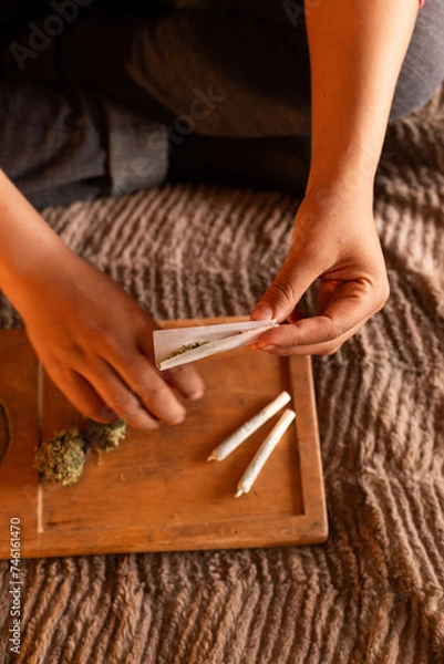 Obraz A person is seen skillfully preparing a handmade weed cigarette. Their fingers carefully work the paper, shaping it with precision