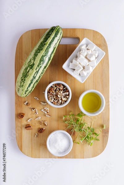 Fototapeta Cucumber Salad with White Cheese and Nuts Ingredients on a wooden chopping board and white background