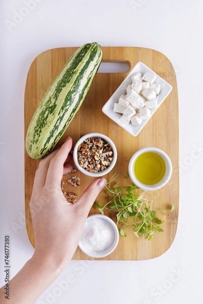 Fototapeta Cucumber Salad with White Cheese and Nuts Ingredients on a wooden chopping board and white background