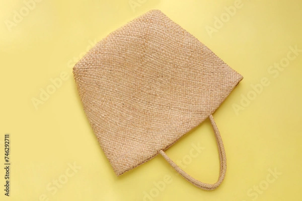 Obraz Brown wicker woven bag or straw bag on yellow background. Top view with copy space. Summer travel concept. 