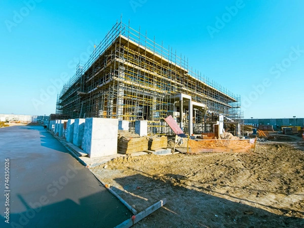 Fototapeta Scaffolding at the construction site of a multi-storey building. construction site with scaffolding and building materials, blue sky background