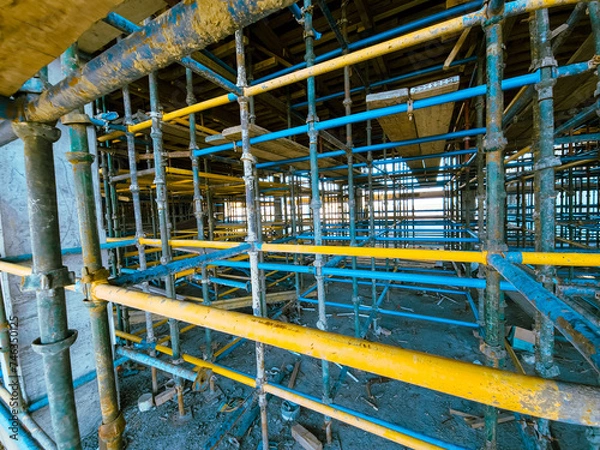 Fototapeta Scaffolding at the construction site of a multi-storey building. construction site with scaffolding and building materials, blue sky background