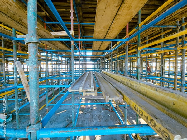 Fototapeta Scaffolding at the construction site of a multi-storey building. construction site with scaffolding and building materials, blue sky background