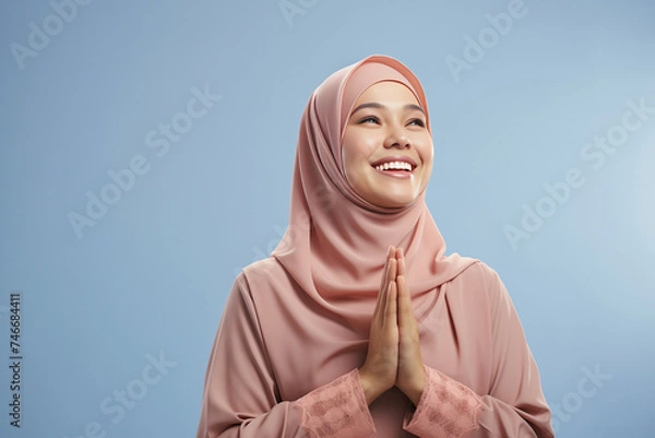 Obraz Beautiful Asian Muslim woman with a radiant smile, making an Eid Mubarak greeting gesture, isolated on a clean background, representing the concept of religious lifestyle