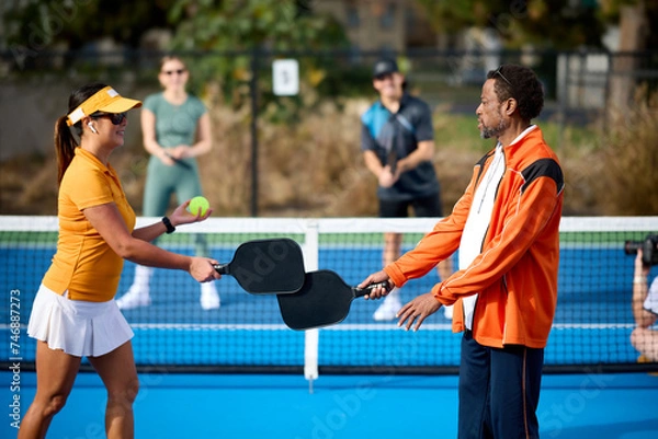 Obraz A mixed group of pickleball players plays on a blue court during the day