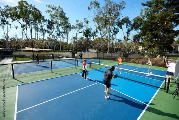 Fototapeta Two pickleball courts with athletes playing games with long shadows.